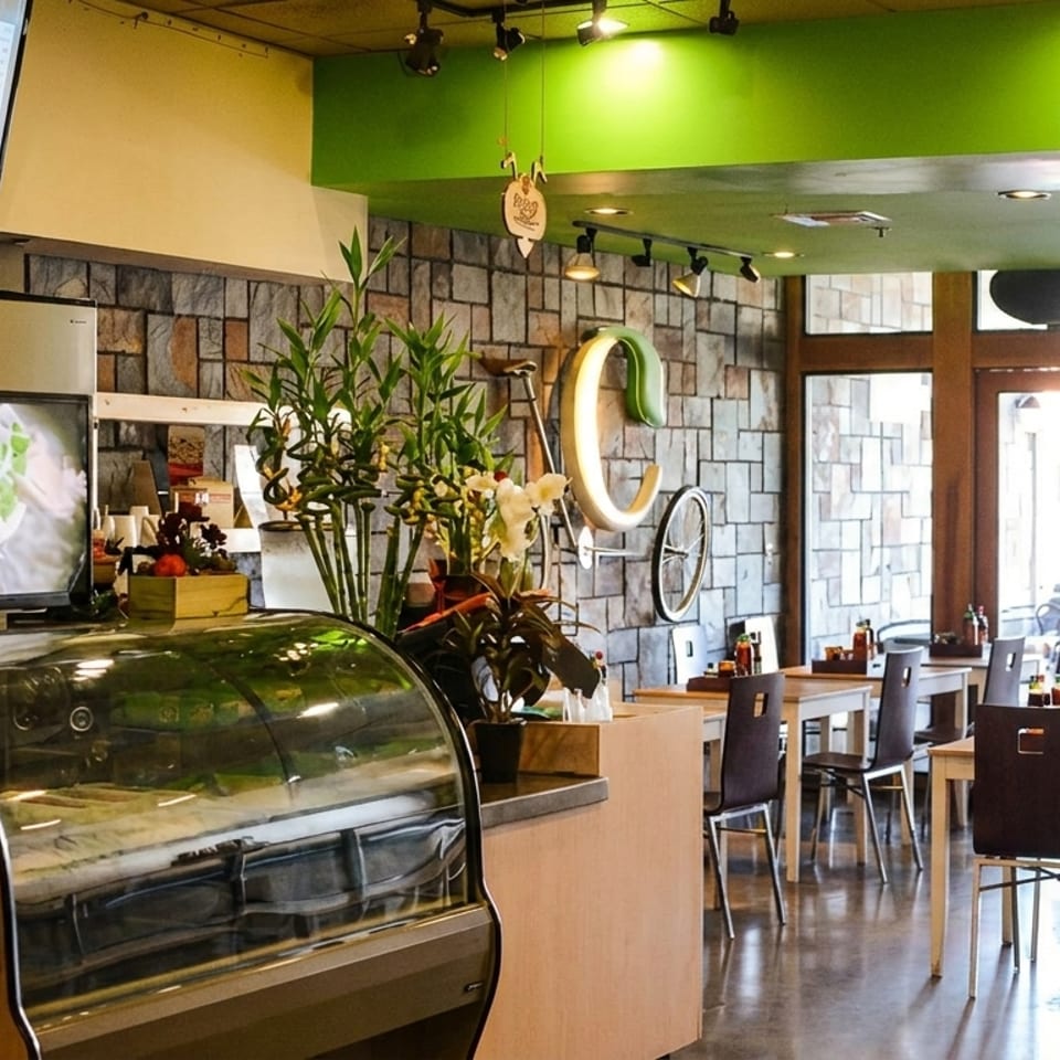 Interior of a modern restaurant with stone walls, green ceiling accents, and wooden tables and chairs.
