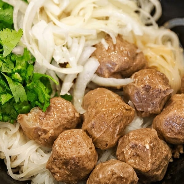 Close-up of a bowl of pho with noodles, beef meatballs, sliced onions, and fresh cilantro.