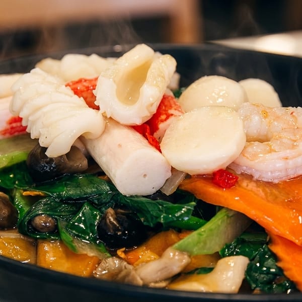 Steaming hot seafood and vegetable stir-fry with shrimp, squid, and crab sticks in a black bowl.