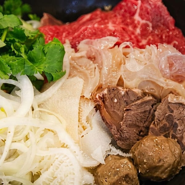 A bowl of pho ingredients including raw beef, tripe, onions, and cilantro.