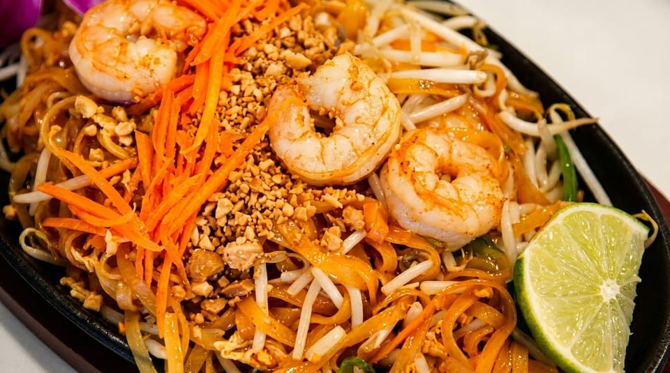Shrimp Pad Thai with noodles, bean sprouts, carrots, crushed peanuts, and a lime wedge.