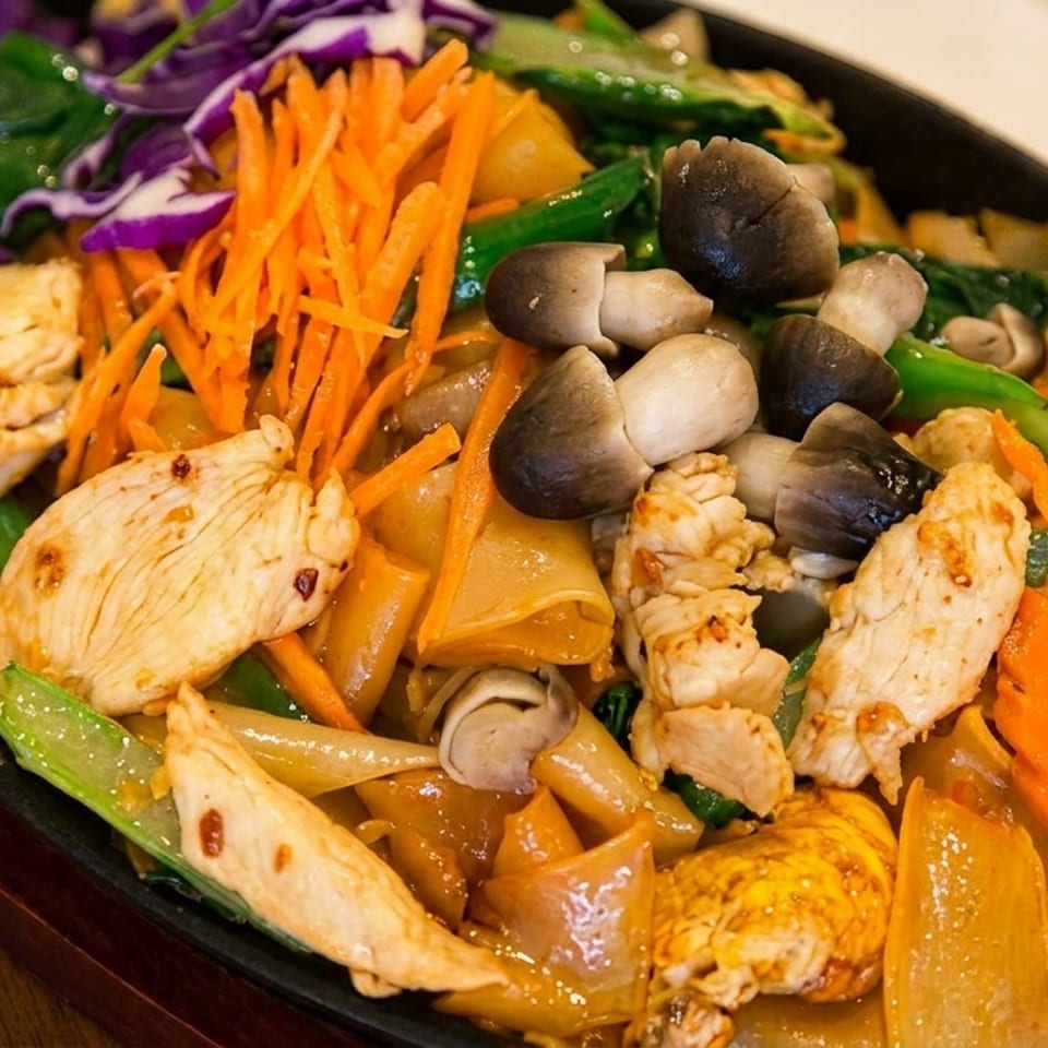 Sizzling chicken and vegetable stir-fry with wide noodles, mushrooms, carrots, and purple cabbage.