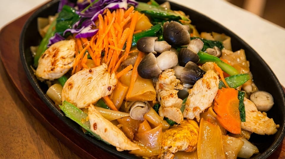 Sizzling chicken and vegetable stir-fry with wide noodles, mushrooms, carrots, and purple cabbage.